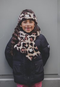 Zwarte gewatteerde jas, sjaal van luipaardprint en haarband. De sjaal valt om de nek, de haarband ligt op het haar, beide hebben een zachte textuur.