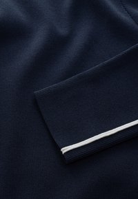 Mørk marineblåt strikket stof med en foldet manchet, der har en enkelt tynd hvid stribe nær kanten.