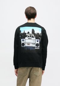 Μαύρη φούτερ μπλούζα με μια πολύχρωμη γραφική εικόνα ενός μπούμπαξ και φόντο με τον ουρανοξύστη, που αναδεικνύει μια λεπτομερή σχεδίαση και υφασμάτινη υφή.