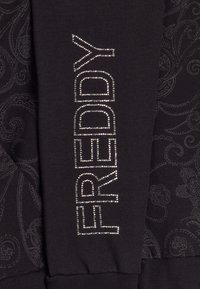 Un tissu noir présente un motif paisley texturé. Le mot "FREDDY" est orné de strass argentés sur le côté.