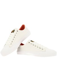 Baskets en toile blanches avec semelles en caoutchouc, bout rond et œillets en argent. L'intérieur a une doublure orange, avec un label logo sur la languette.