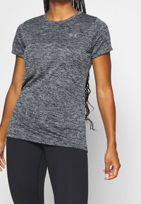 Szara melanżowa koszulka sportowa z krótkimi rękawami, okrągłym dekoltem i logo Under Armour. Połączona z czarnymi legginsami o gładkiej fakturze.