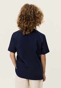 Μπλε ναυτικό βαμβακερό μπλουζάκι με κοντά μανίκια, στρογγυλεμένο γιακά και ίσια γραμμή. Διαθέτει μικρή ετικέτα με λογότυπο στο τελείωμα.