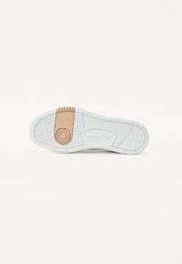Sål af en sneakers med en hvid gummibase, fiskebensmønster og en tan accent med prægede logo på hælen.