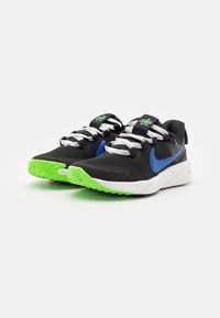 Black athletic shoes with a ridged texture, featuring a blue swoosh, green accents, and white laces. The sole is bright green with traction details.