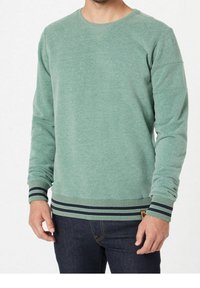 Sudadera verde con escote redondo, puños acanalados con rayas marinas y tejido texturizado, combinada con jeans de mezclilla oscura.
