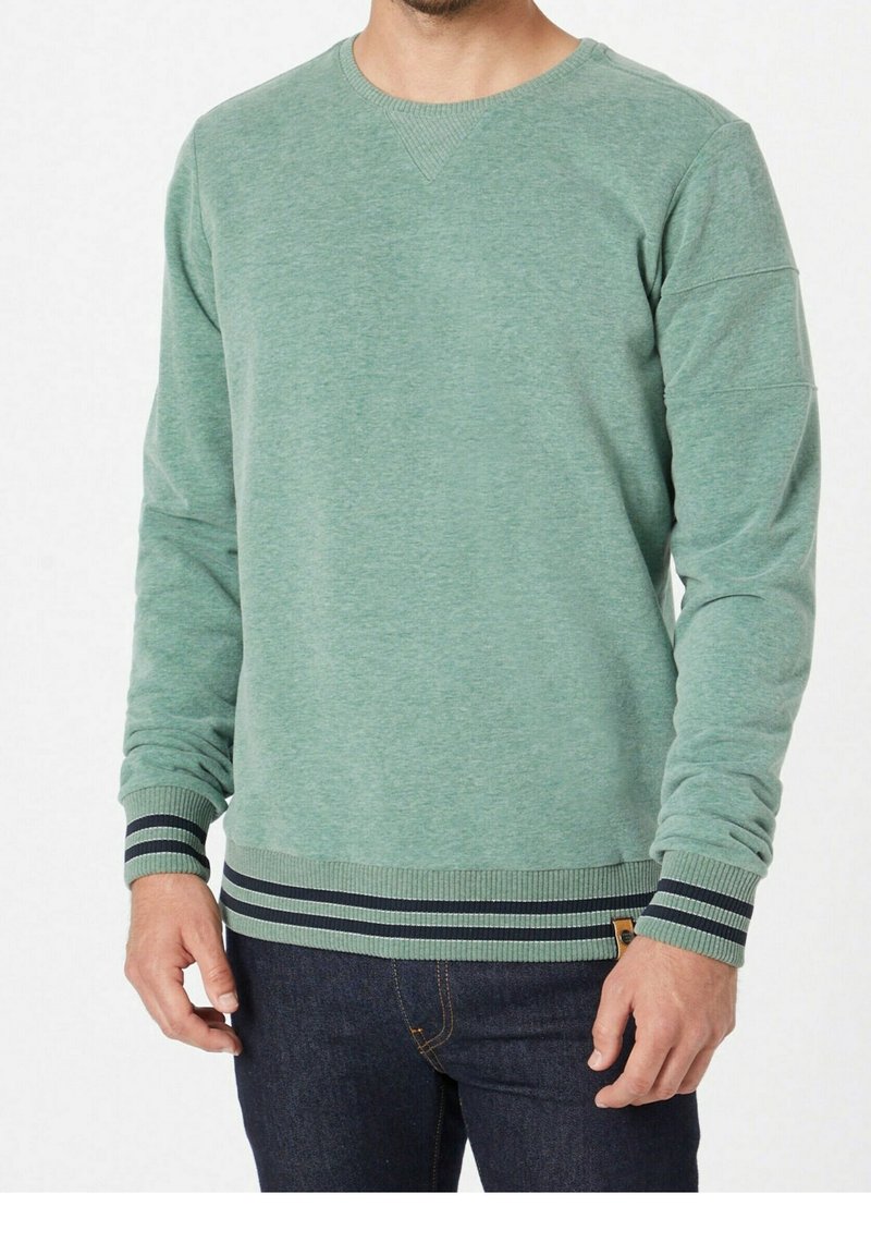 Sudadera verde con escote redondo, puños acanalados con rayas marinas y tejido texturizado, combinada con jeans de mezclilla oscura.