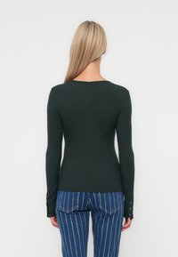 Mørkegrønn ribbet langermet topp med rund hals og knappe-accenter ved mansjettet, kombinert med blå vertikale stripete jeans.