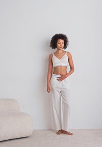 Un crop top gris clair avec des fines bretelles, associé à un pantalon de pyjama blanc avec de subtiles rayures verticales. Texture de tissu douce, design minimaliste.