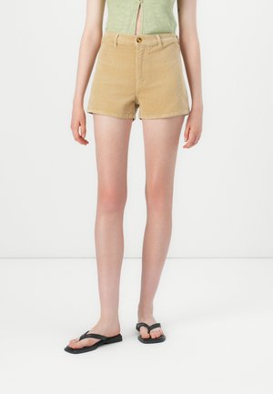Beige corduroy shorts with a high waist, front button closure, and two side pockets. Paired with black flip-flops. Smooth texture.