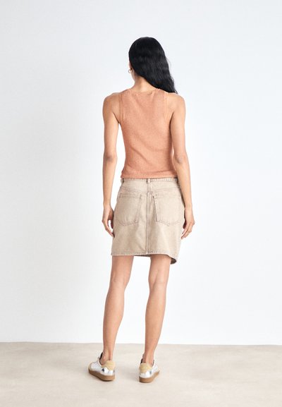 Un débardeur côtelé beige associé à une mini-jupe en denim crème avec des poches et un ourlet brut, complété par des baskets décontractées.