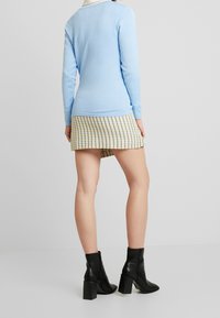 Světle modrý dlouhý rukáv top spárovaný s kostkovanou mini sukní v žluté a černé barvě, doplněný černými kotníkovými botami na podpatku.