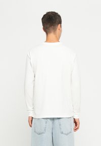 Maglietta bianca a maniche lunghe in cotone, con una vestibilità comoda, scollatura rotonda e design minimalista, abbinata a pantaloni shorts in denim azzurri.