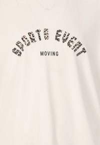 Hvid t-shirt med v-hals. Har en leopardprint tekst "SPORTS EVENT" der buer over ordet "MOVING" i fed sorte bogstaver.
