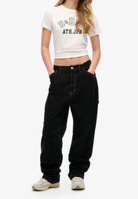 Pantalones de pierna ancha negros con costuras blancas en contraste, que cuentan con bolsillos laterales y una cintura alta. Combinados con una camiseta gráfica blanca corta.