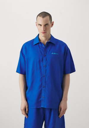 Koszula z krótkim rękawem z jasnoniebieskiego materiału, z wyraźnym kołnierzykiem, haftem oraz luźnym krojem.