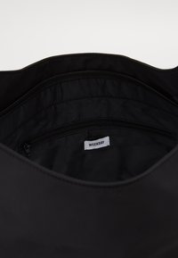 Schwarze Stofftasche mit glatter Innenfläche, Reißverschlusstasche und sichtbarem "WEEKDAY"-Label. Das Design ist einfach und funktional.