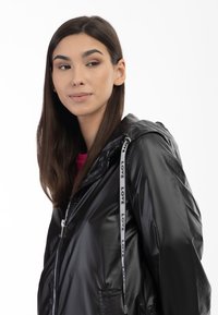 Zwarte hoodie met glanzende stof, rits aan de voorkant, zakken en trekkoorden met de tekst "LOVE" langs de rand.