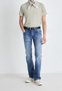 Camisa polo gris claro, pantalones vaqueros de mezclilla azul, cinturón negro, zapatillas blancas y una bufanda estampada. Corte recto con un leve desgaste en los jeans.