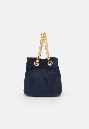 Marineblå flettet spandtaske med to tykke guldkædehåndtag, der trækkes gennem guldfarvede øjer.