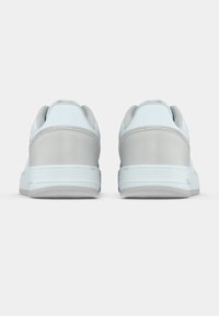 Λευκά και γκρι αθλητικά παπούτσια με λείο δερμάτινο επάνω μέρος, επενδεδυμένο γιακά και υφασμένο λαστιχένιο πέλμα, παρουσιάζοντας έναν μινιμαλιστικό σχεδιασμό.