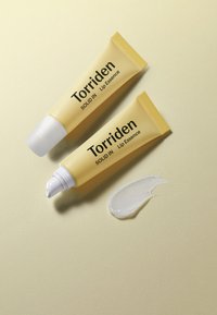To gule squeeze tuber af Torriden Solid In Lip Essence med hvide skruelåg; den ene tube dispenserer klar lip essence på en lys baggrund.