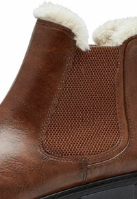Bottines en cuir marron avec un panneau latéral élastique texturé et une doublure douce et duveteuse le long du bord supérieur pour plus de confort.