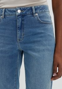 Vaaleansiniset farkut, joissa on korkea vyötärö, metallinen nappikiinnitys, etutaskut ja hienovarainen haalistuma kankaassa.