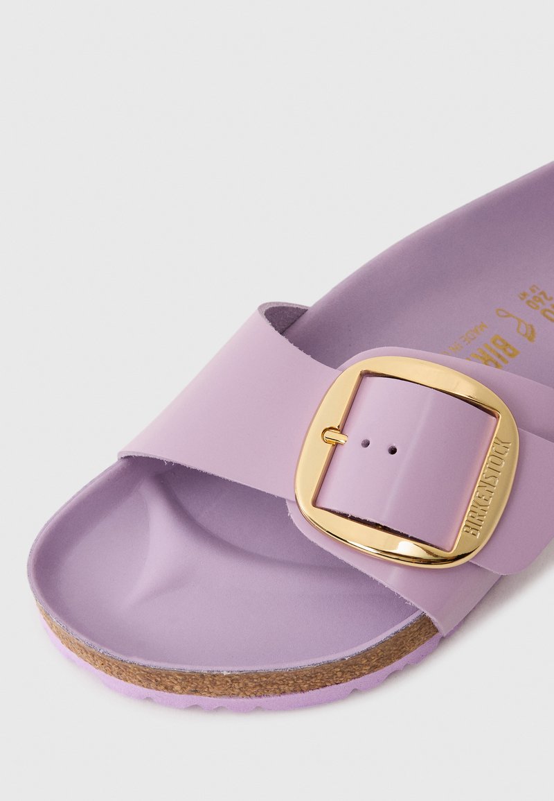 Hell lilafarbene Birkenstock-Sandale mit einem breiten Riemen, goldener Schnalle und Korksohle. Glatte Textur mit konturiertem Fußbett und verstellbarem Verschluss.