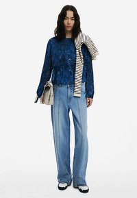 Mėlynas, tekstūruotas ilgomis rankovėmis viršus, laisvi džinsai, balti juodi batai, ant peties užmestas dryžuotas megztinis.