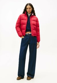 Rød pufferjakke med quiltet design, høj krave og lynlås. Sammen med mørkeblå wide-leg jeans og sko med leopardprint.