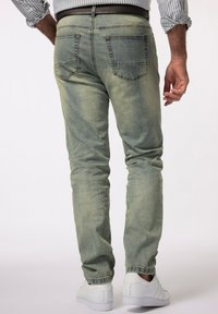 Jeans de mezclilla verde claro deslavado con corte slim, que presentan bolsillos traseros clásicos y un diseño de tobillo cónico, combinados con zapatillas blancas.