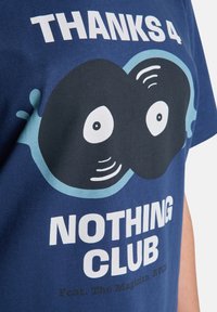Μπλε βαμβακερό T-shirt με γραφικό σχέδιο δύο στυλιζαρισμένων βινυλίων και κείμενο: "THANKS 4 NOTHING CLUB." Χρησιμοποιούνται λευκά και μαύρα χρώματα.