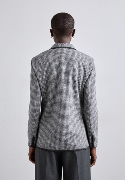 Blazer noir et gris à motif pied-de-poule avec un col cranté, ajustement slim et manches tailleur. Comprend des fentes latérales et une texture lisse.