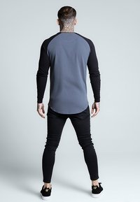 T-shirt à manches raglan longues en gris avec des manches noires, fabriqué dans un tissu doux. Associé à un pantalon noir ajusté et des baskets noires basses.
