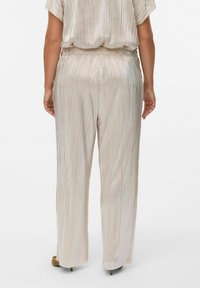 Pantalons plissés à jambes larges en tissu beige clair avec un éclat métallique. Taille élastique et texture lisse. Pas de motifs ou d'accents distincts.