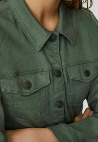 Grön denimjacka med klassisk krage, knappstängning, två bröstfickor och textil med synlig sömnad.