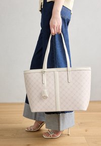 Sac fourre-tout en matière rose pâle à motifs avec des accents blancs, doté d'une forme structurée, de bretelles d'épaule et d'un détail charmant.