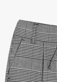 Šedé a černé kostkované kalhoty s texturovanou tkaninou, s plochým pasem a bočními kapsami. Vzor obsahuje houndstooth a kostkované designy.