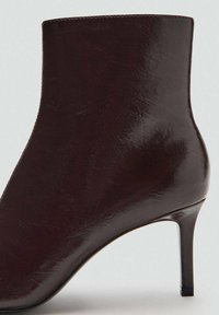 Bottine en cuir bordeaux au design épuré, à bout pointu et talon aiguille fin. Texture lisse avec des détails de couture minimaux.