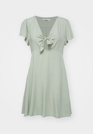 Kratký rukáv, áčková šaty vo svetlozelenej farbe s predným uzlom a textúrovanou tkaninou. Plynulý strih, dĺžka po kolená.
