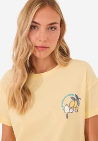 T-shirt di cotone gialla con maniche corte, caratterizzata da una grafica di un limone e un personaggio, con testo stampato "Se la vita ti dà limoni."