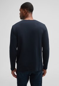 Marineblaues Langarm-T-Shirt aus weichem Stoff, mit Rundhalsausschnitt und geradem Saum. Getragen mit dunkelblauen Jeans, minimales Detail.