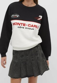 Zwart-wit sweatshirt met rode accenten, met de tekst "MONTE-CARLO CÔTE D'AZUR". Gecombineerd met een plissé zwarte denim rok.