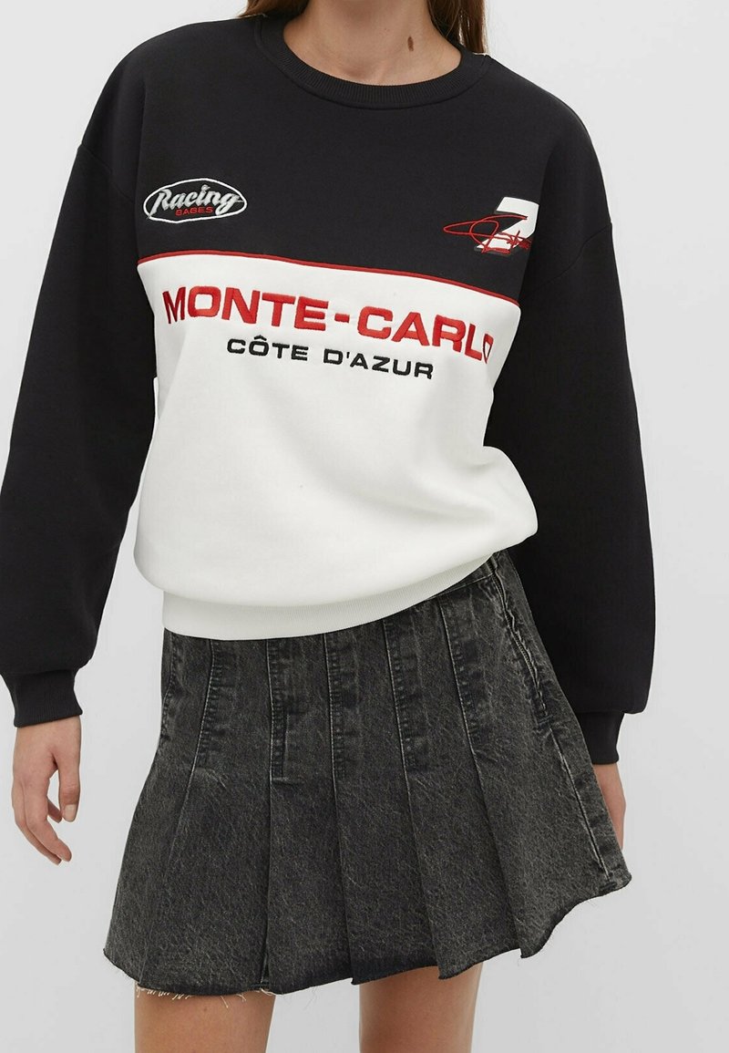 Zwart-wit sweatshirt met rode accenten, met de tekst "MONTE-CARLO CÔTE D'AZUR". Gecombineerd met een plissé zwarte denim rok.