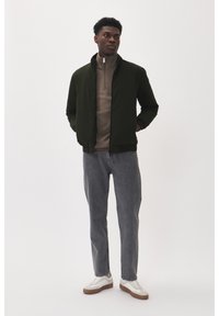 Dunkelgrüne Bomberjacke, beige Zip-up-Oberteil, graue Jeans und weiße Sneaker mit braunen Sohlen. Schlichtes, lässiges und tailliertes Design.