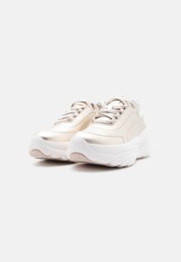 Ζευγάρι μπεζ chunky sneakers με παχιά λευκή σόλα και κορδόνια, τοποθετημένα δίπλα-δίπλα σε απλό λευκό φόντο.