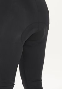 Svarta leggings med en slät textur, som har en konturerad passform och elastisk midja. Förstärkt sömnad längs sömmarna för hållbarhet.