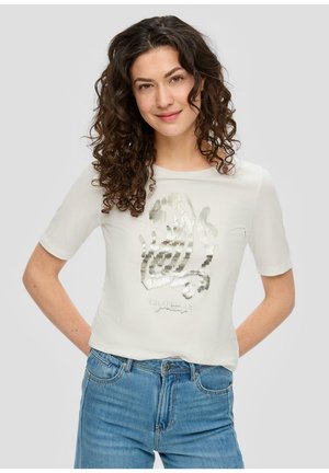 T-shirt blanc à manches courtes avec un design graphique argent métallisé et du texte sur le devant. Associé à un jean en denim bleu.