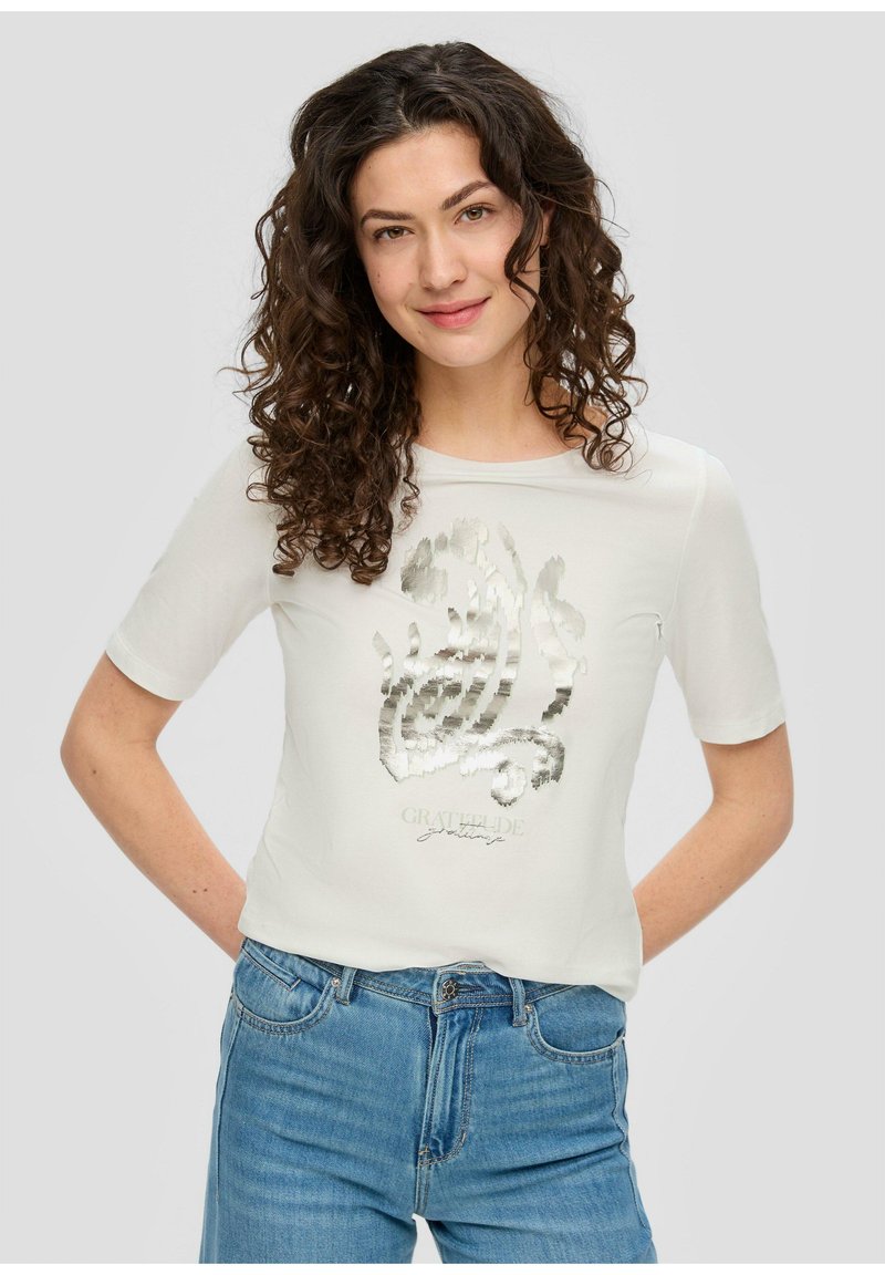 Witte t-shirt met korte mouwen met een metallic zilveren grafisch ontwerp en tekst aan de voorkant. Gecombineerd met blauwe denim jeans.